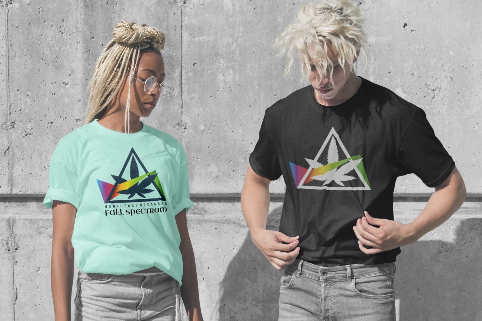 Two people wearing NEA Full Spectrum tees, one mint green and one black, against a concrete wall.